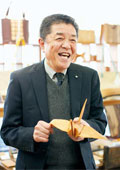 歩く広告塔を自認する谷口正晴社長。バッグやペンケースなどBOISブランドを愛用する。手にするのは「縫える木」で作った折り鶴　写真