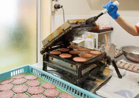 プレハブの作業場内で「能登いか煎餅」を焼いているところの写真。作業場は震災後に工場の隣に建てた。