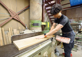 倒壊した工場から運び込んだ機械で、木材の表面を削る寺田さんの写真。